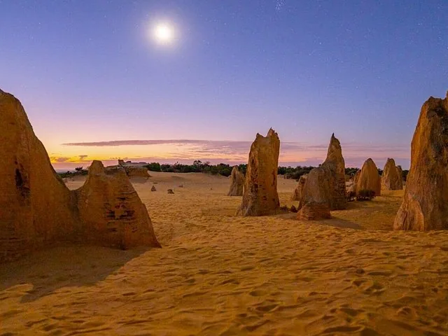 Moon shining brightly over the limestone formations in the Pinnacles Desert at dusk.