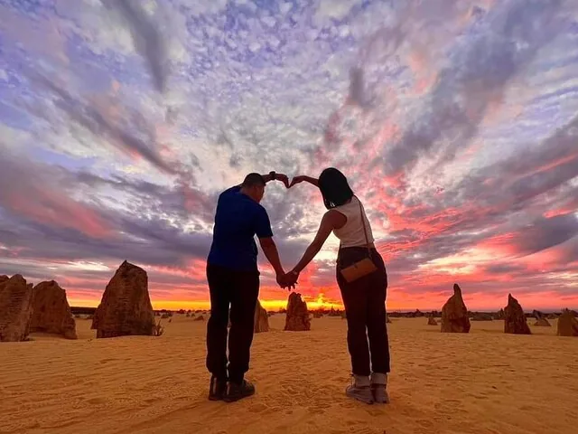Paar, das bei Sonnenuntergang in der Pinnacles-Wüste mit den Armen ein Herz formt.