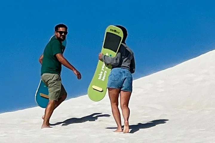 Un uomo e una donna che portano sandboard su una duna di sabbia bianca.