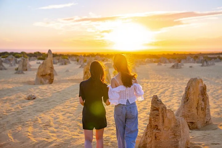 Two women walking among the limestone formations at sunset in the Pinnacles Desert.