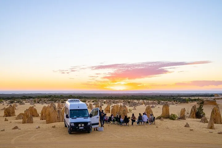 Gruppo di persone sedute vicino a un van bianco al tramonto nel Deserto dei Pinnacles.