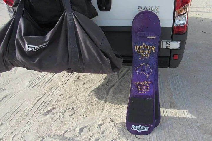 Purple sandboard and a black bag leaning against the back of a van.